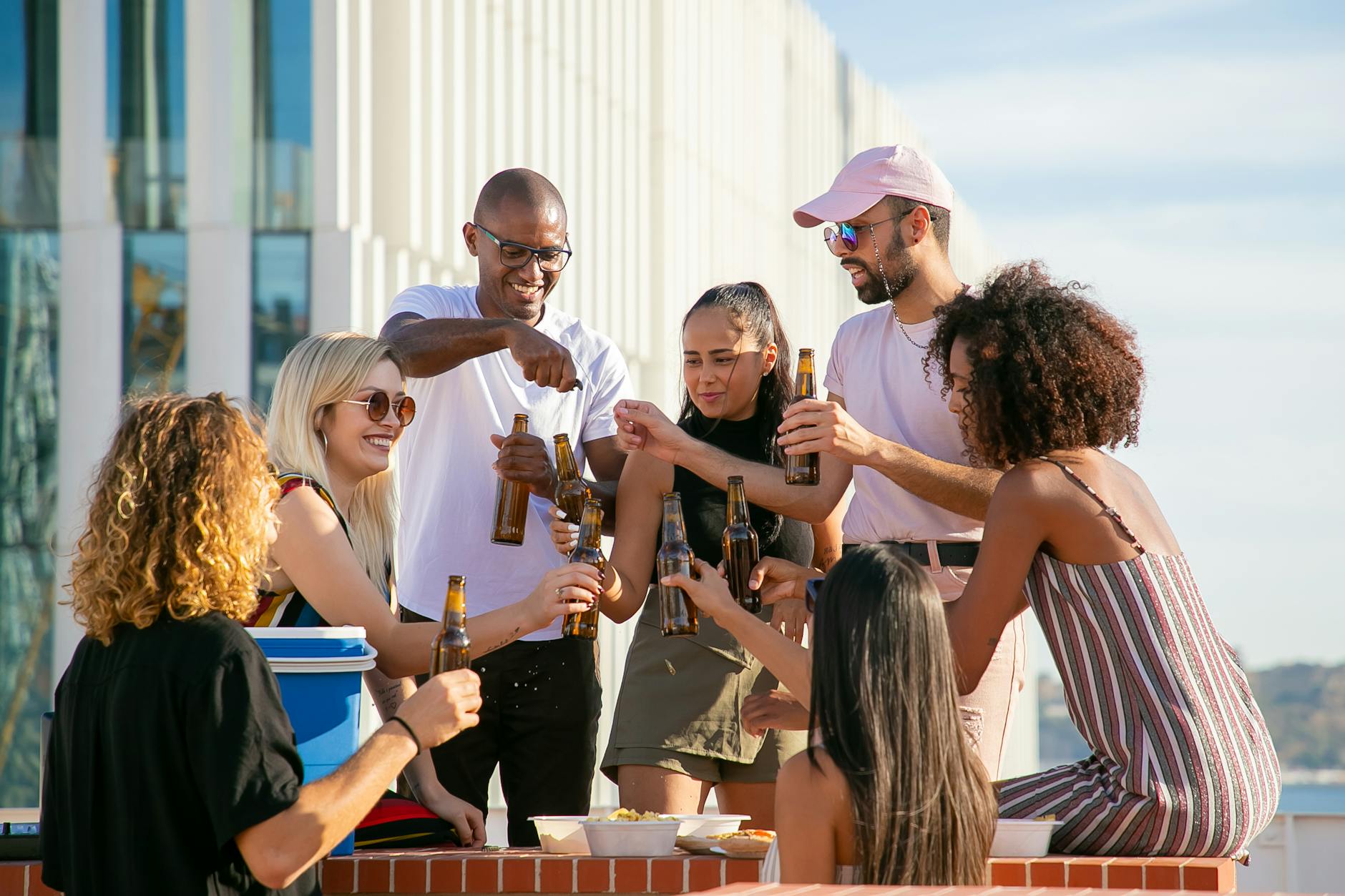 happy diverse friends clinking bottles on terrace