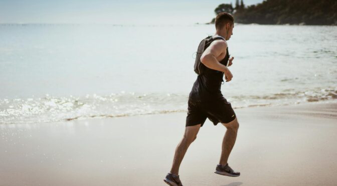 man wearing black tank top and running on seashore